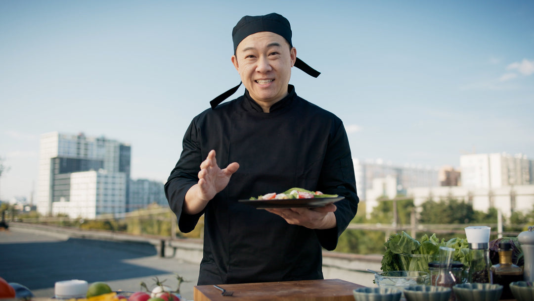 Cook wearing black headwear and holding a plate of food outdoors