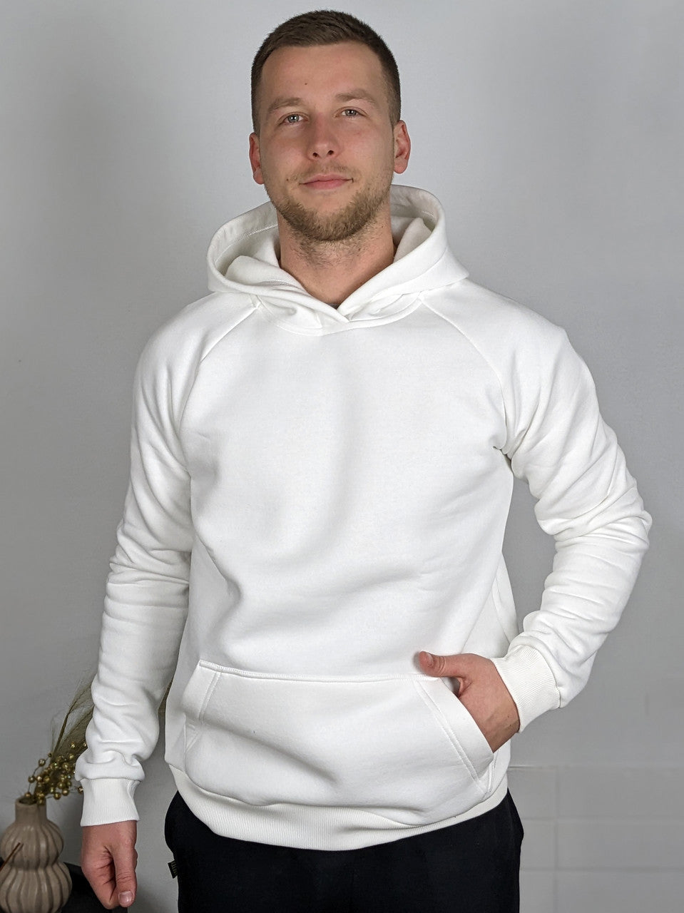 A man wearing a white insulated hoodie with a kangaroo pocket, standing in a casual pose.