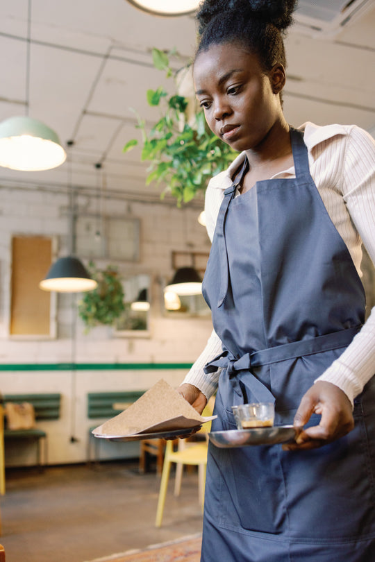 Waitress wearing a dark gray bib apron while serving coffee in a café