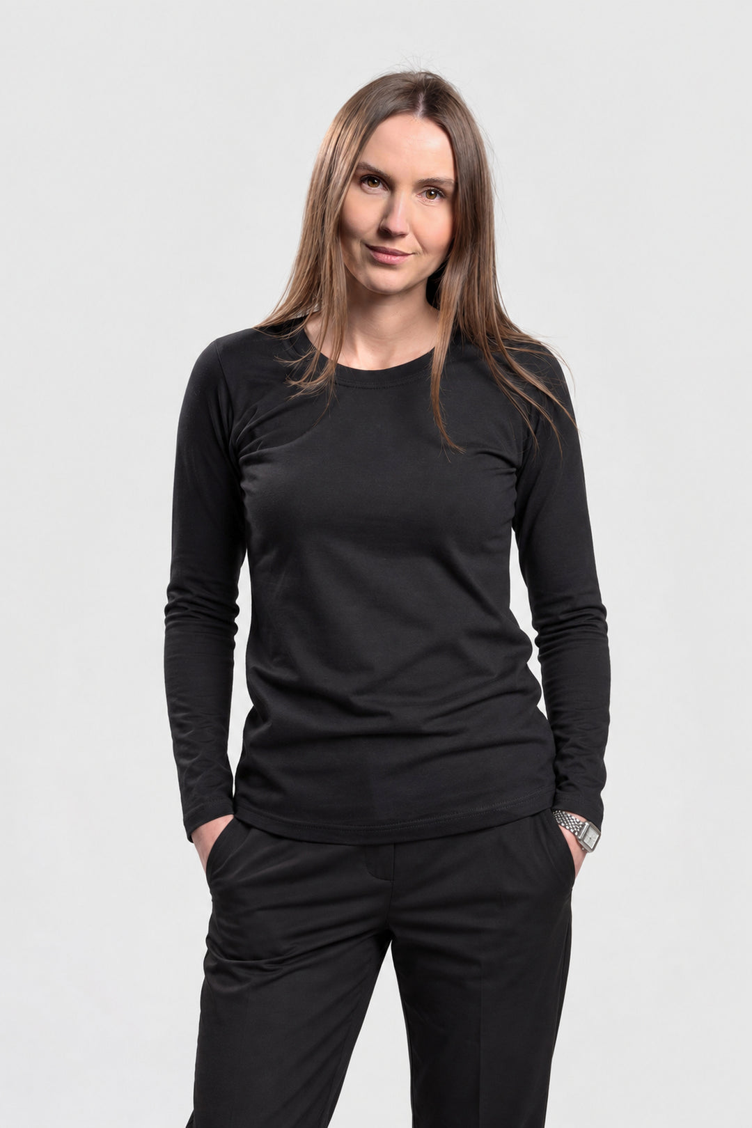 A woman modeling a black long-sleeve crewneck shirt and matching black pants against a light gray studio background.