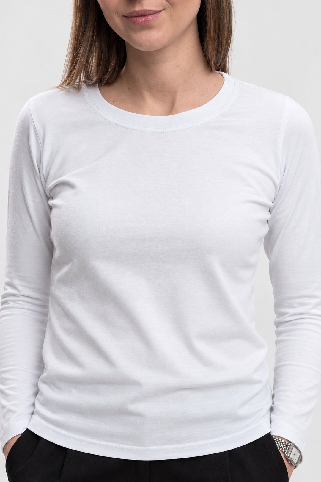 A woman wearing a plain white long-sleeve crewneck t-shirt, cropped from the chin down, against a light gray studio background.