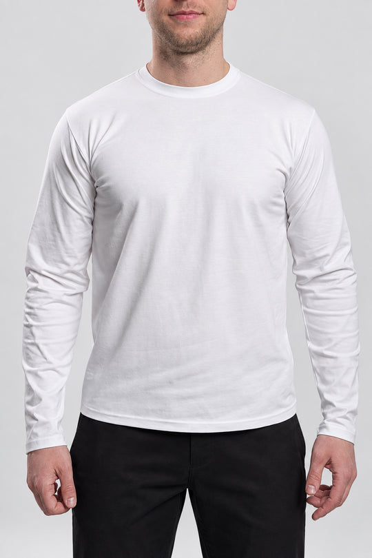 A man wearing a plain white long-sleeve crewneck t-shirt and black pants, shown from the chin down against a light gray studio background.