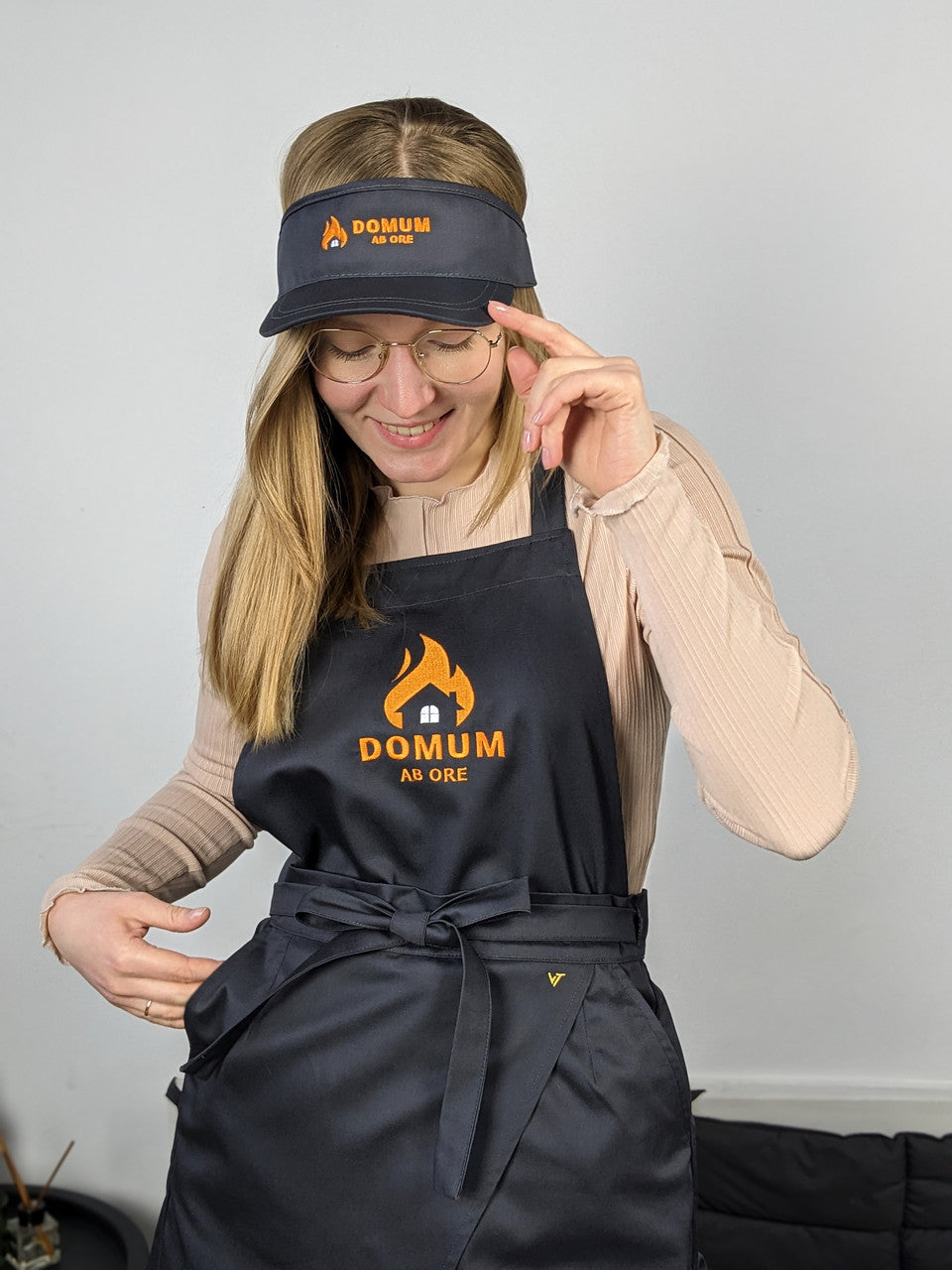 A person wearing a dark grey visor cap with a logo on it, and a matching apron.