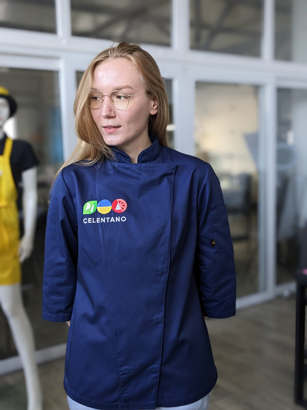 A person wearing a green chef coat with a logo on the chest.