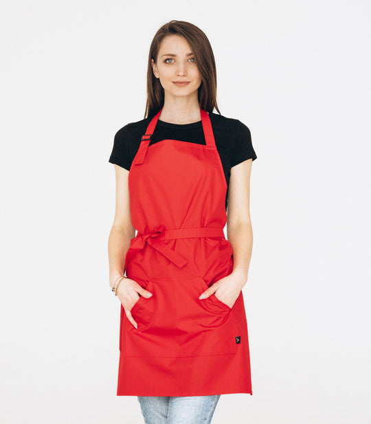 A person wearing a red, full-length apron with pockets, in a standing pose.
