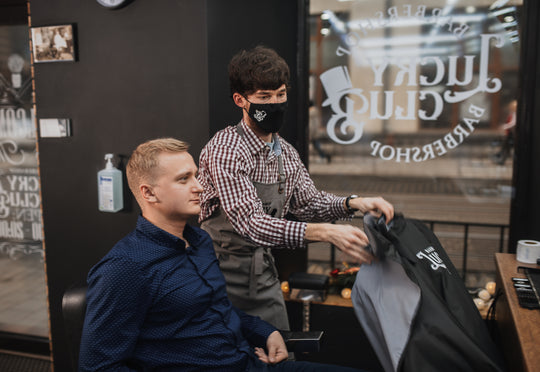 Barber wearing a gray pinstripe apron while preparing a cape for a client