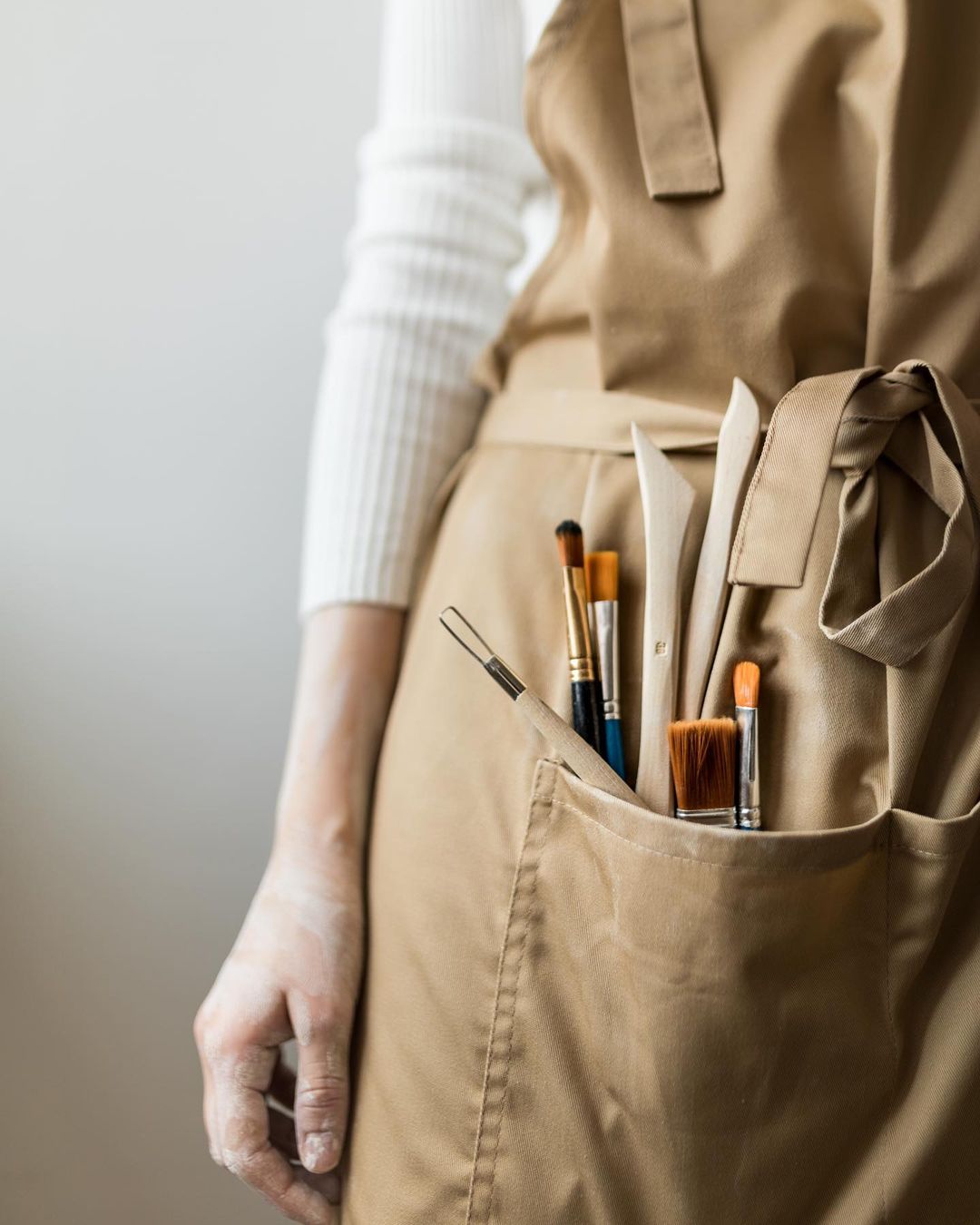 Beige bib apron with pockets holding brushes and pottery tools
