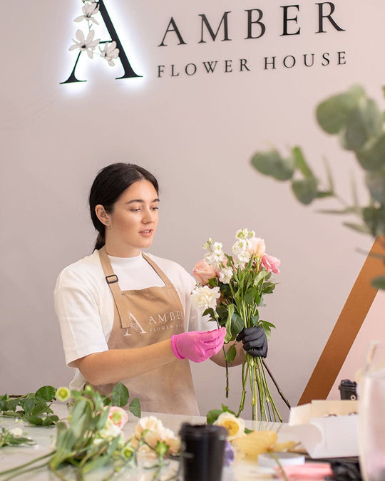Florist wearing a beige bib apron with logo while arranging flowers