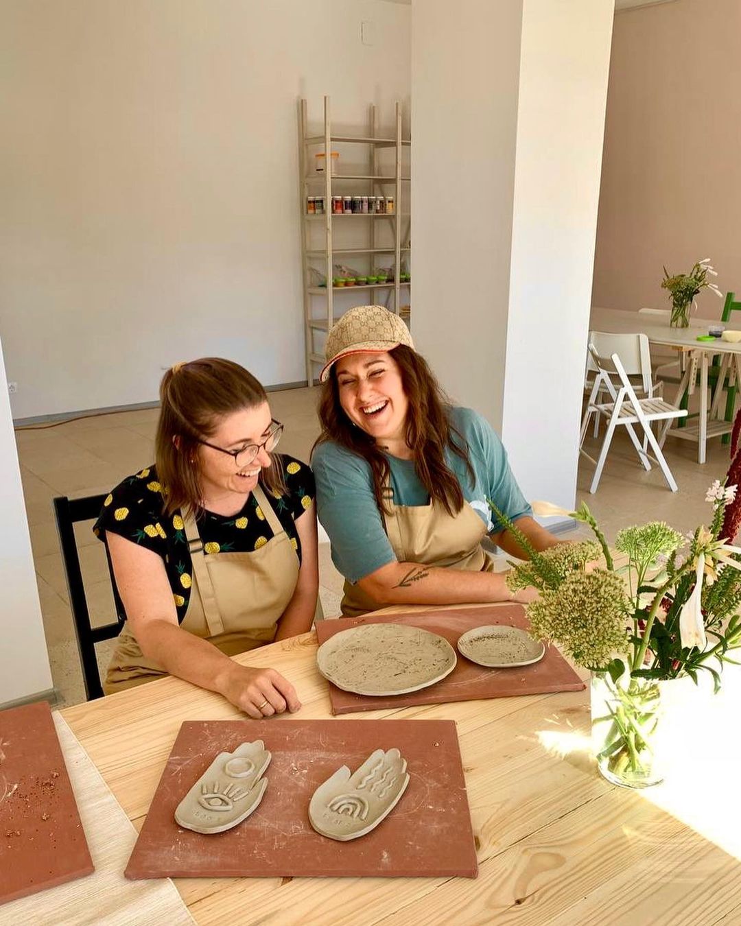 Two women wearing beige bib aprons during a pottery workshop