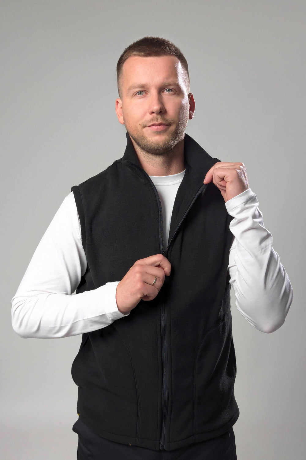 Man wearing a black vest over a white shirt on a gray background