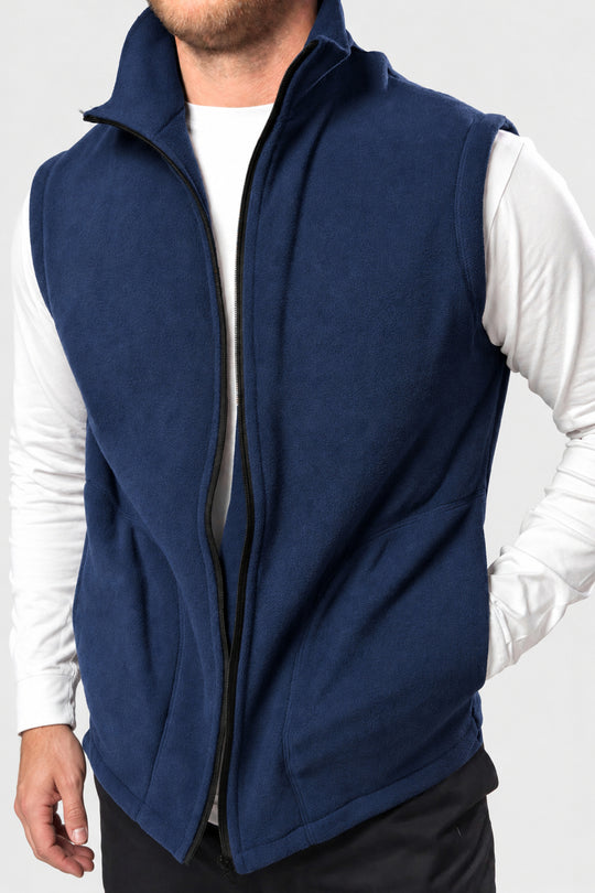 A man wearing a navy blue zip-up fleece vest over a white long-sleeve shirt, shown from the neck down against a light gray background.