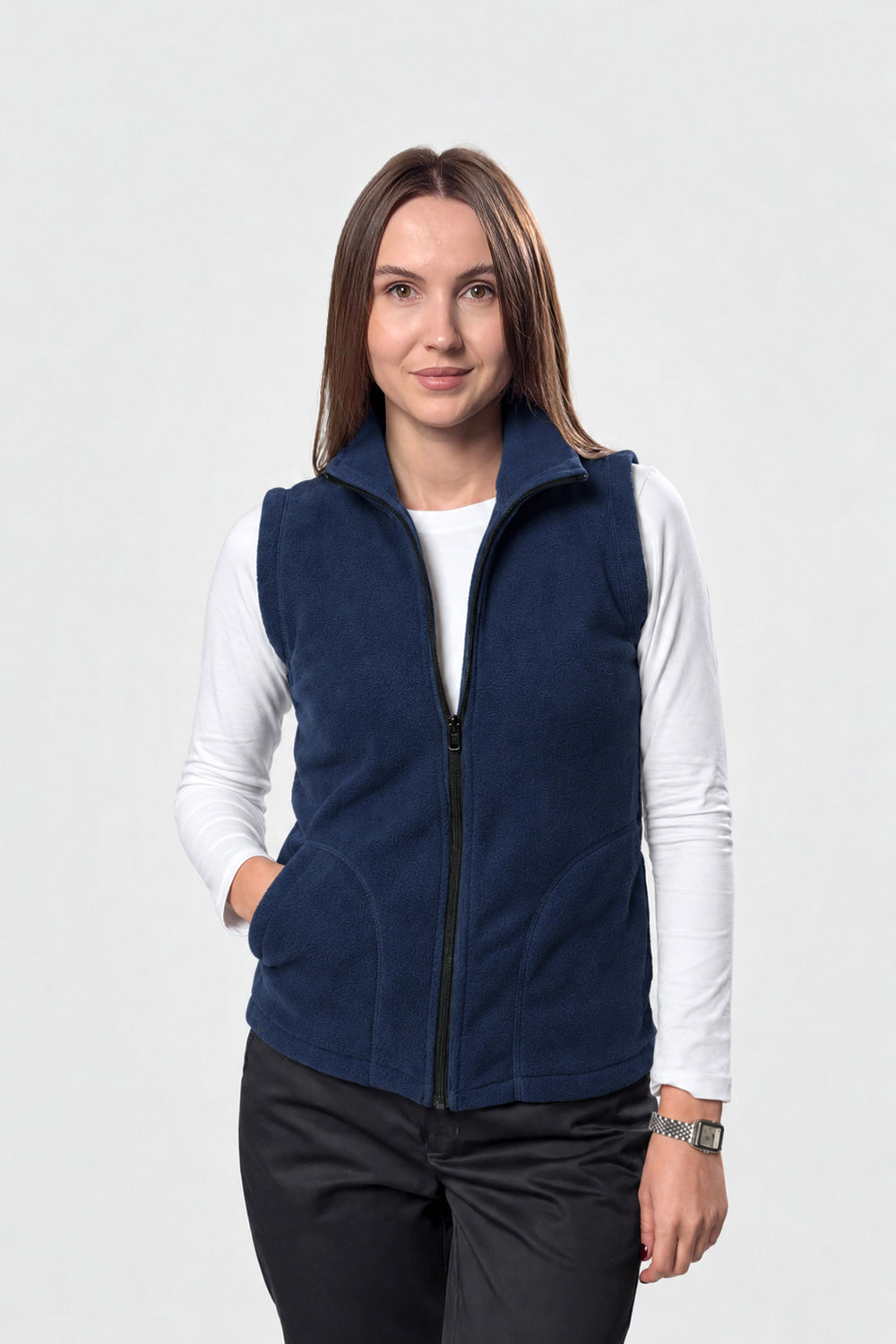 A woman modeling a navy blue zip-up fleece vest over a white long-sleeve shirt and black pants, photographed against a light gray studio background.