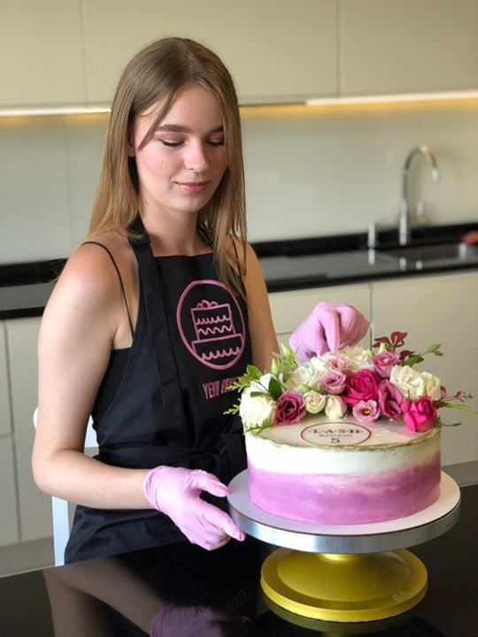 Baker wearing a black bib apron with logo while decorating a floral cake