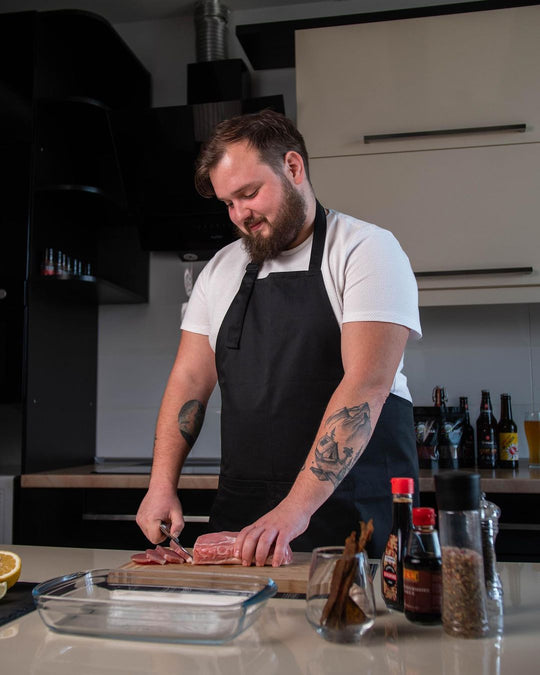 Man wearing a black bib apron while preparing food in a kitchen