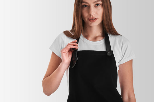 Woman wearing a black bib apron with adjustable neck strap and snap fastening