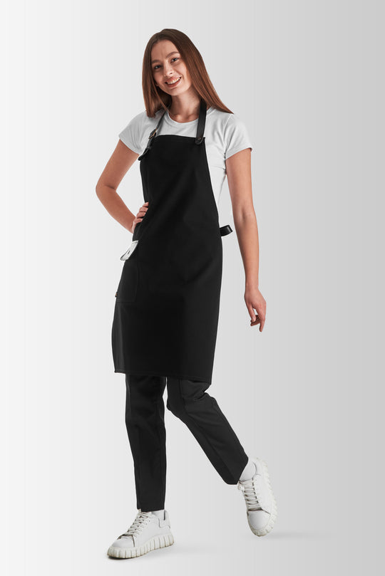 Woman wearing a black bib apron with adjustable black straps and side pocket