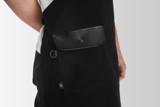 Black bib apron with large front pocket, black flap and metal ring detail