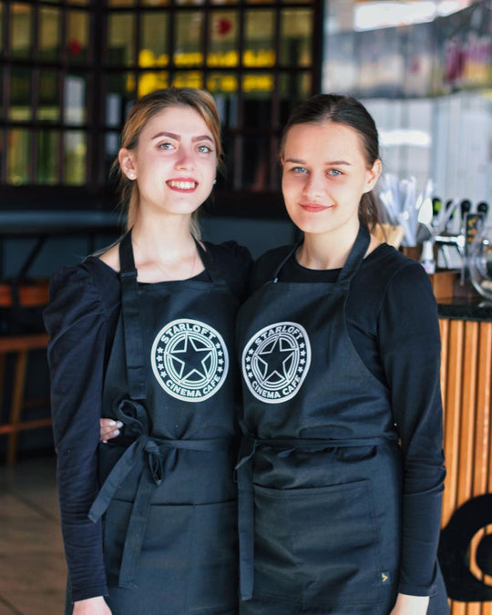 Two restaurant staff wearing black bib aprons with logos