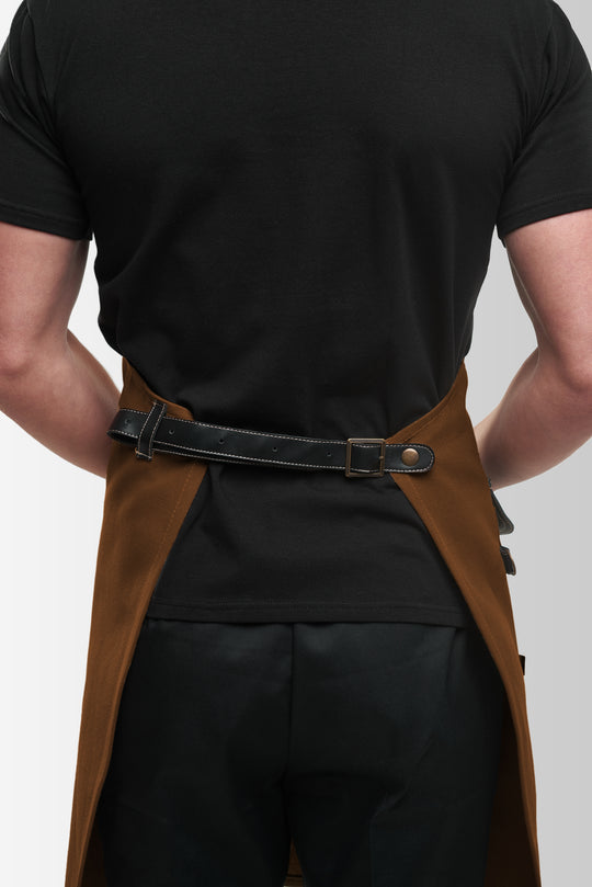 Back view of brown bib apron with adjustable black waist strap and metal buckle