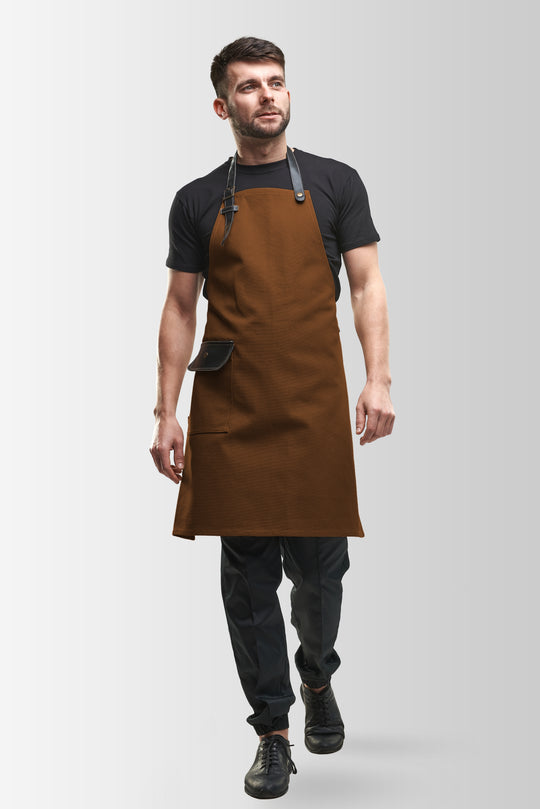 Man wearing a brown bib apron with black adjustable straps and flap pocket