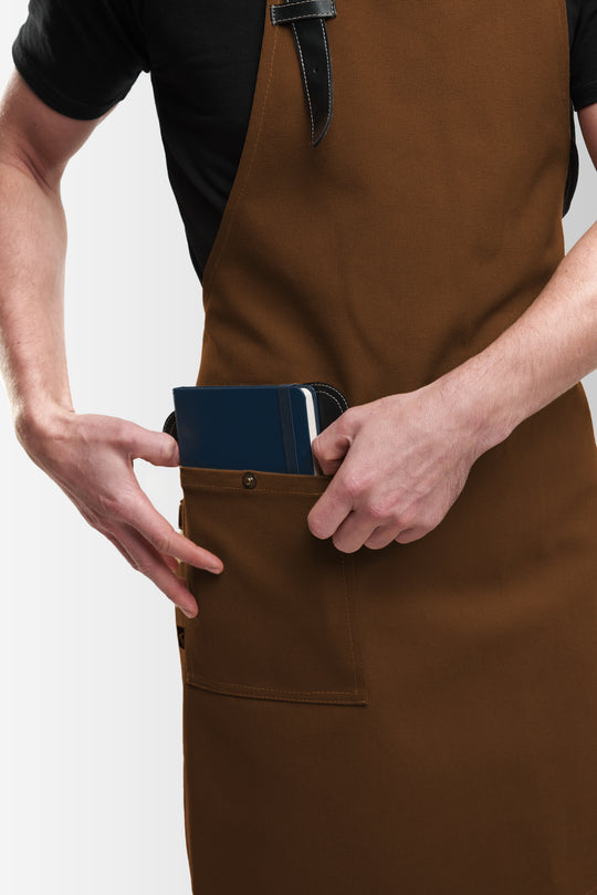 Close-up of brown bib apron with large front pocket holding a notebook