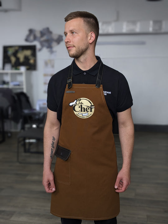Chef wearing a brown bib apron with embroidered logo and black adjustable straps