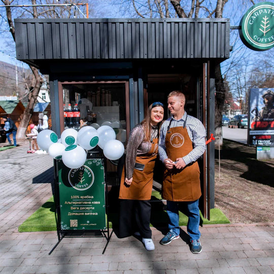 Coffee shop staff wearing brown bib aprons with logos outside a coffee kiosk