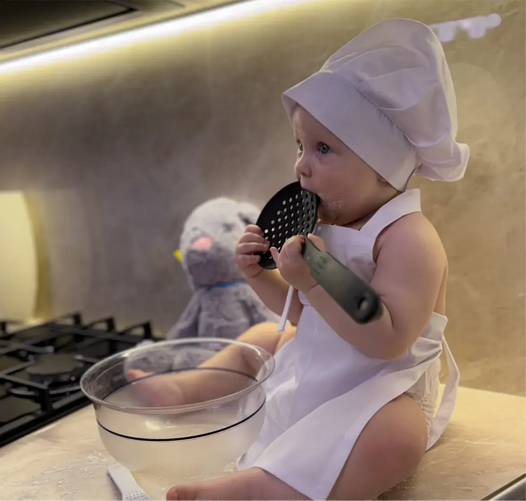 Child wearing a pink chef hat and apron while baking