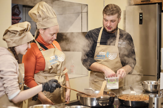 Cooking class participants wearing beige bib aprons with logos while preparing food