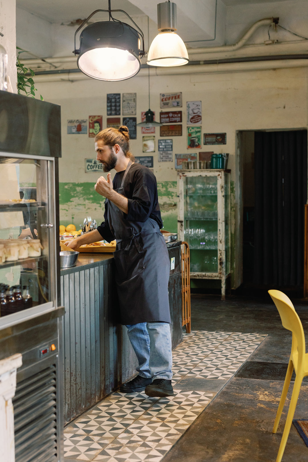 Man wearing a dark gray bib apron while working at a café counter