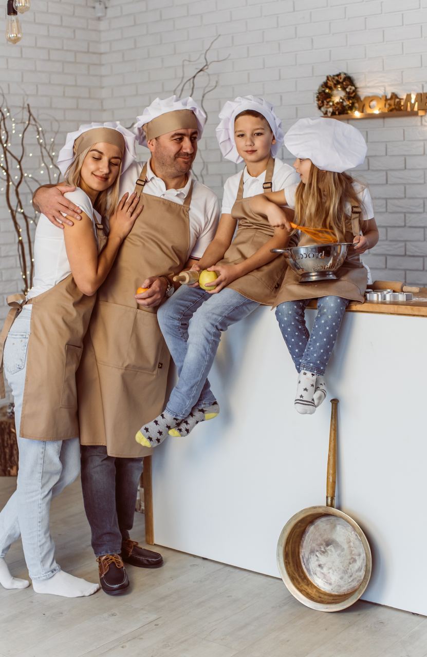 Family wearing beige bib aprons and white chef hats while cooking together