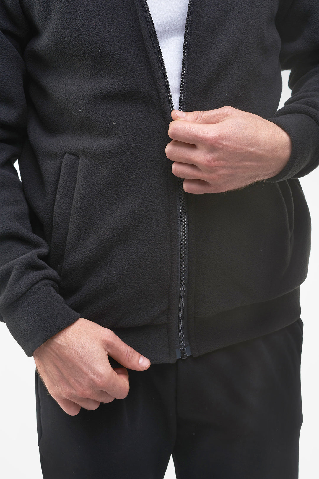 Close-up of a person wearing a black zip-up fleece jacket and matching black pants, with both hands visible adjusting the jacket.