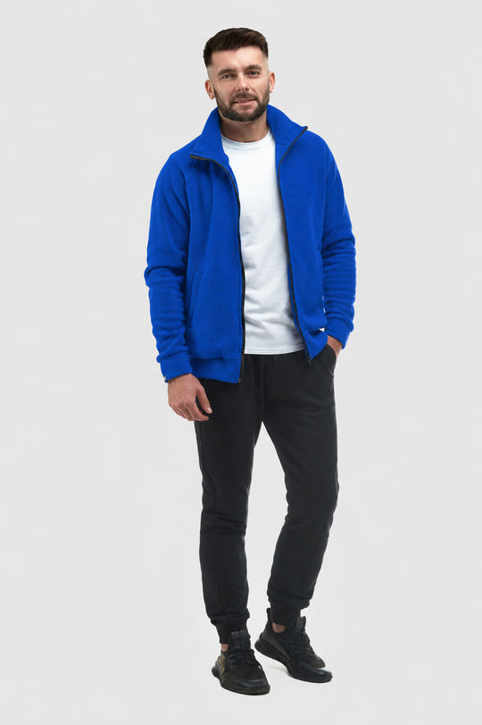A man modeling a bright blue fleece zip-up jacket over a white t-shirt, black jogger pants, and black sneakers, standing against a light gray studio background.