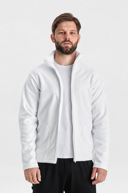 A man wearing a white zip-up fleece jacket over a white t-shirt and black pants, standing against a light gray studio background.