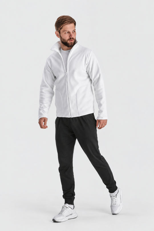A man modeling a white zip-up fleece jacket, black sweatpants, and white sneakers against a light gray studio background.