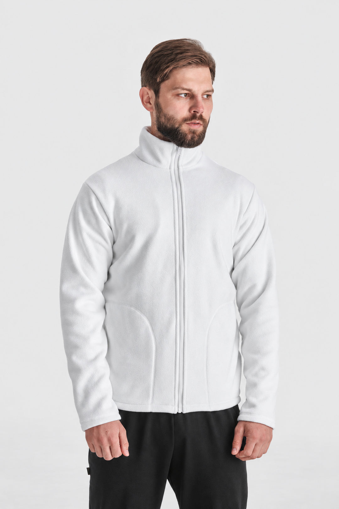 A man wearing a white zip-up fleece jacket and black pants, standing against a light gray studio background.
