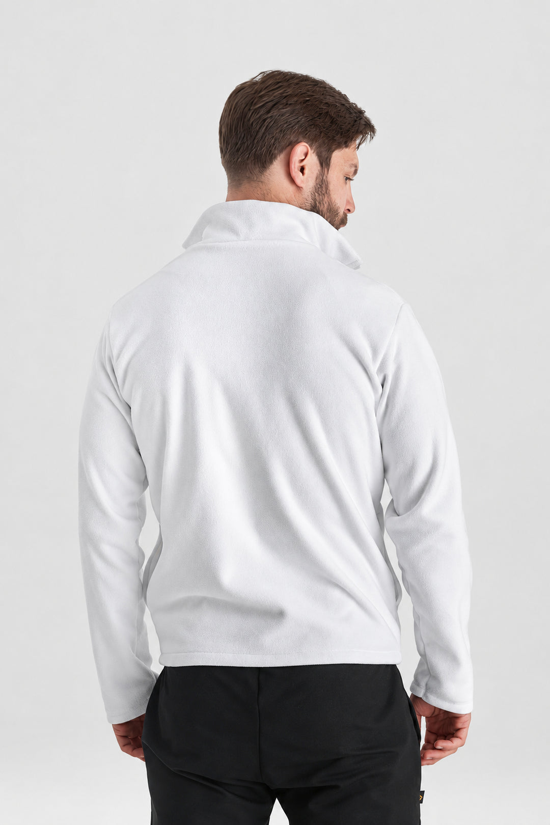 A man viewed from the back wearing a plain white long-sleeve quarter-zip fleece or pullover, paired with black pants, against a light gray studio background.