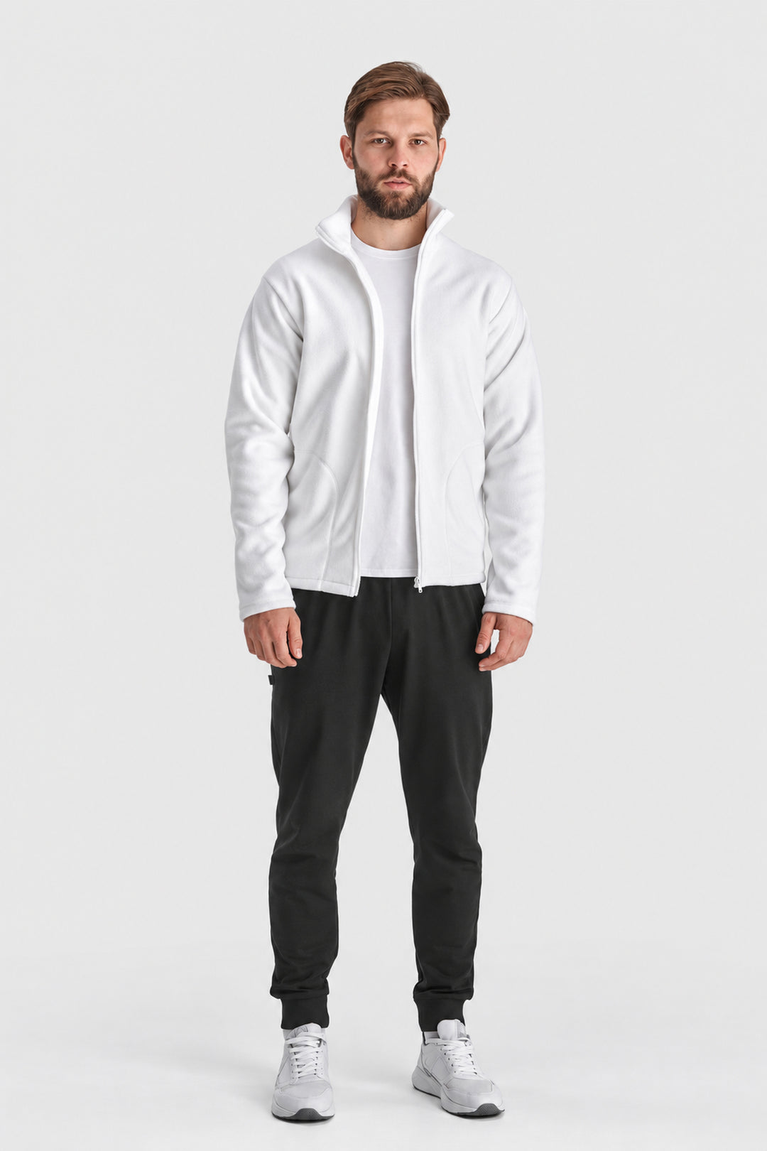 A man modeling a white zip-up hoodie with a high collar, worn over a white t-shirt and black sweatpants, standing against a light gray studio background.