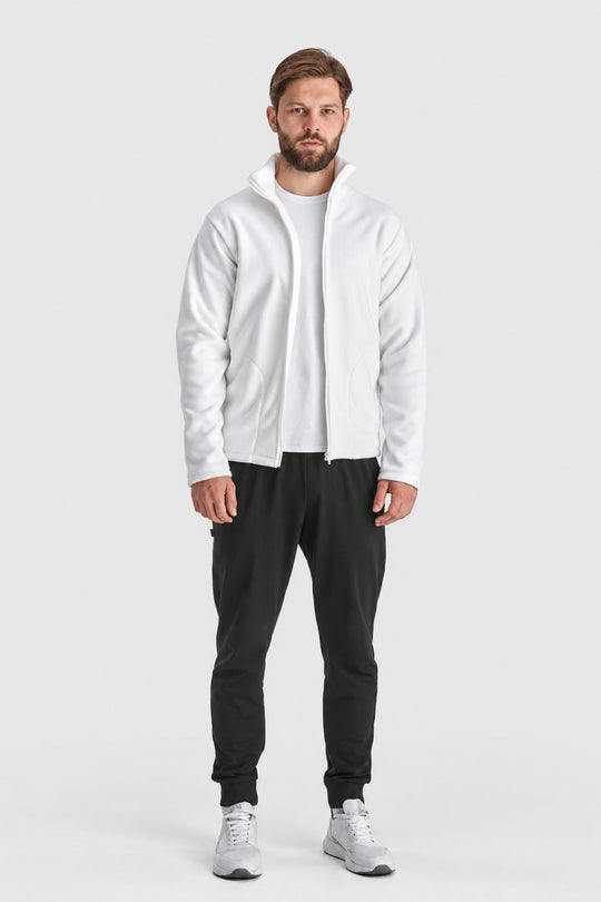 A man modeling a white zip-up hoodie with a high collar, worn over a white t-shirt and black sweatpants, standing against a light gray studio background.