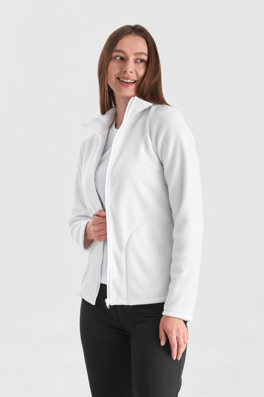 A woman modeling a white zip-up hoodie jacket over a white top and black pants, standing against a light gray studio background.