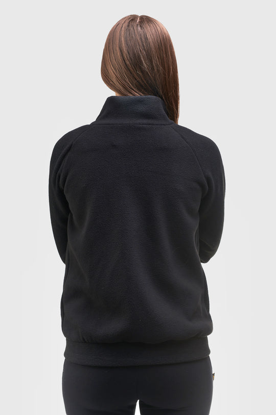 A woman viewed from the back wearing a black long-sleeve quarter-zip fleece jacket and black leggings against a light gray studio background.