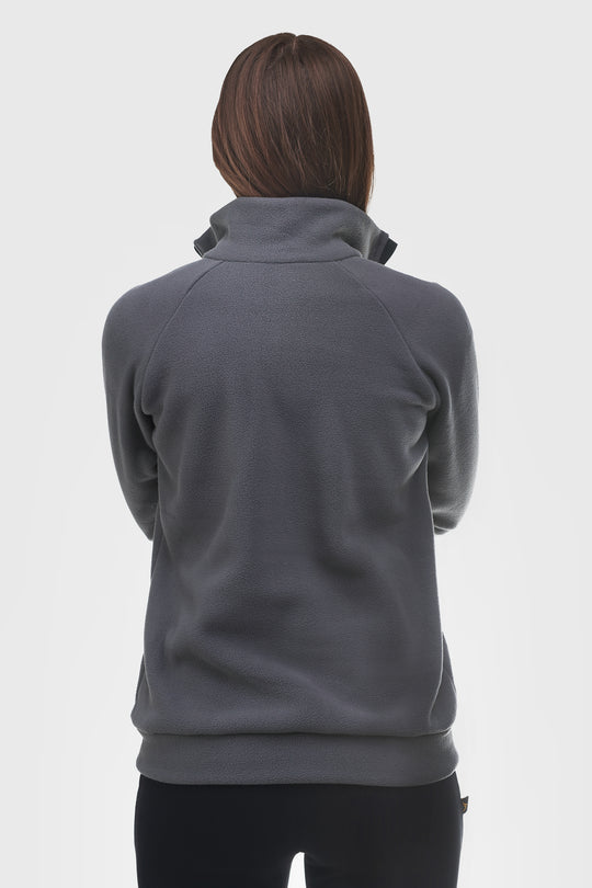 A person shown from the back wearing a dark gray quarter-zip fleece pullover with a mock neck collar and black pants, against a light gray studio background.