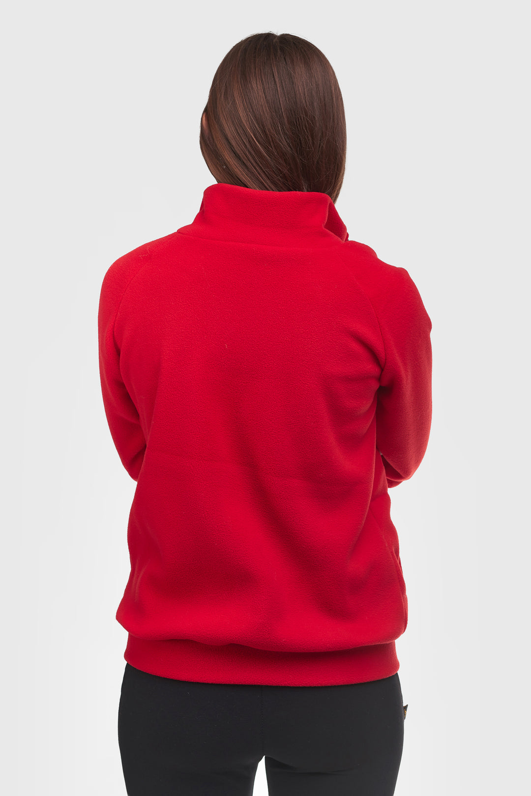 A woman viewed from the back wearing a bright red mock-neck fleece or sweatshirt with black pants, set against a plain light gray studio background.