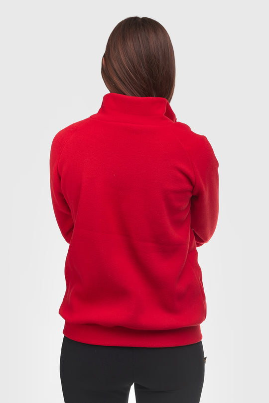 A woman viewed from the back wearing a bright red mock-neck fleece or sweatshirt with black pants, set against a plain light gray studio background.