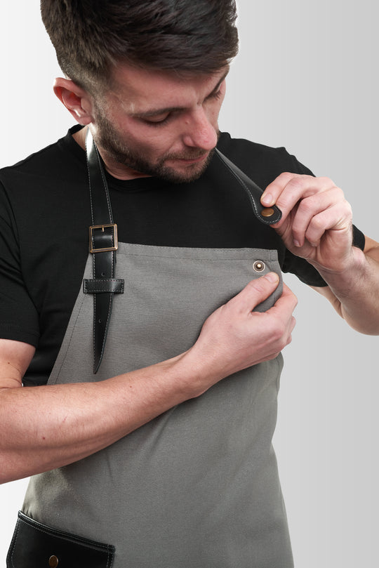 Gray bib apron with adjustable black straps and metal snap fasteners