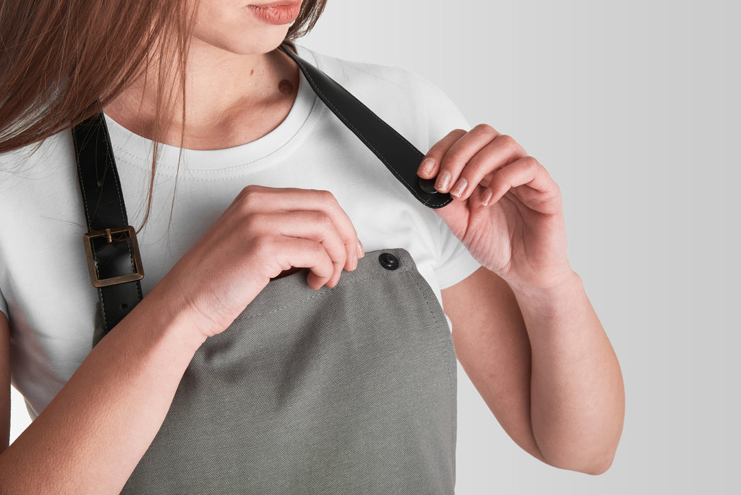 Gray bib apron with detachable black adjustable straps and snap fasteners