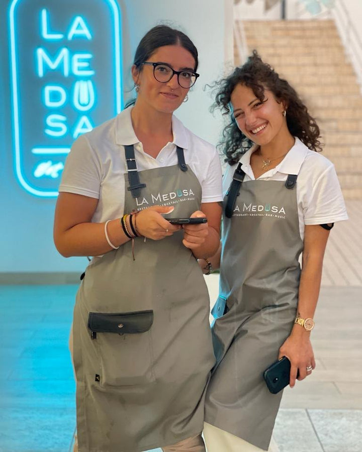 Two restaurant staff wearing gray bib aprons with logos and black adjustable straps