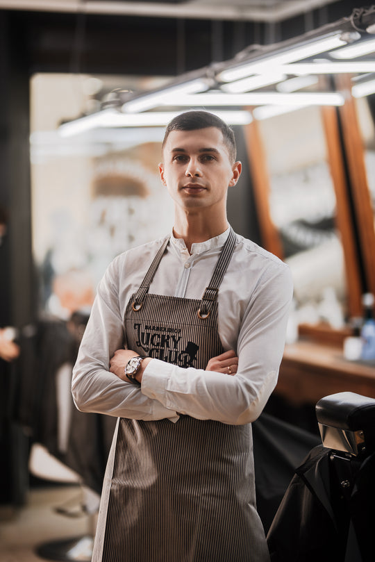 Barber wearing a gray pinstripe bib apron with logo in a barbershop