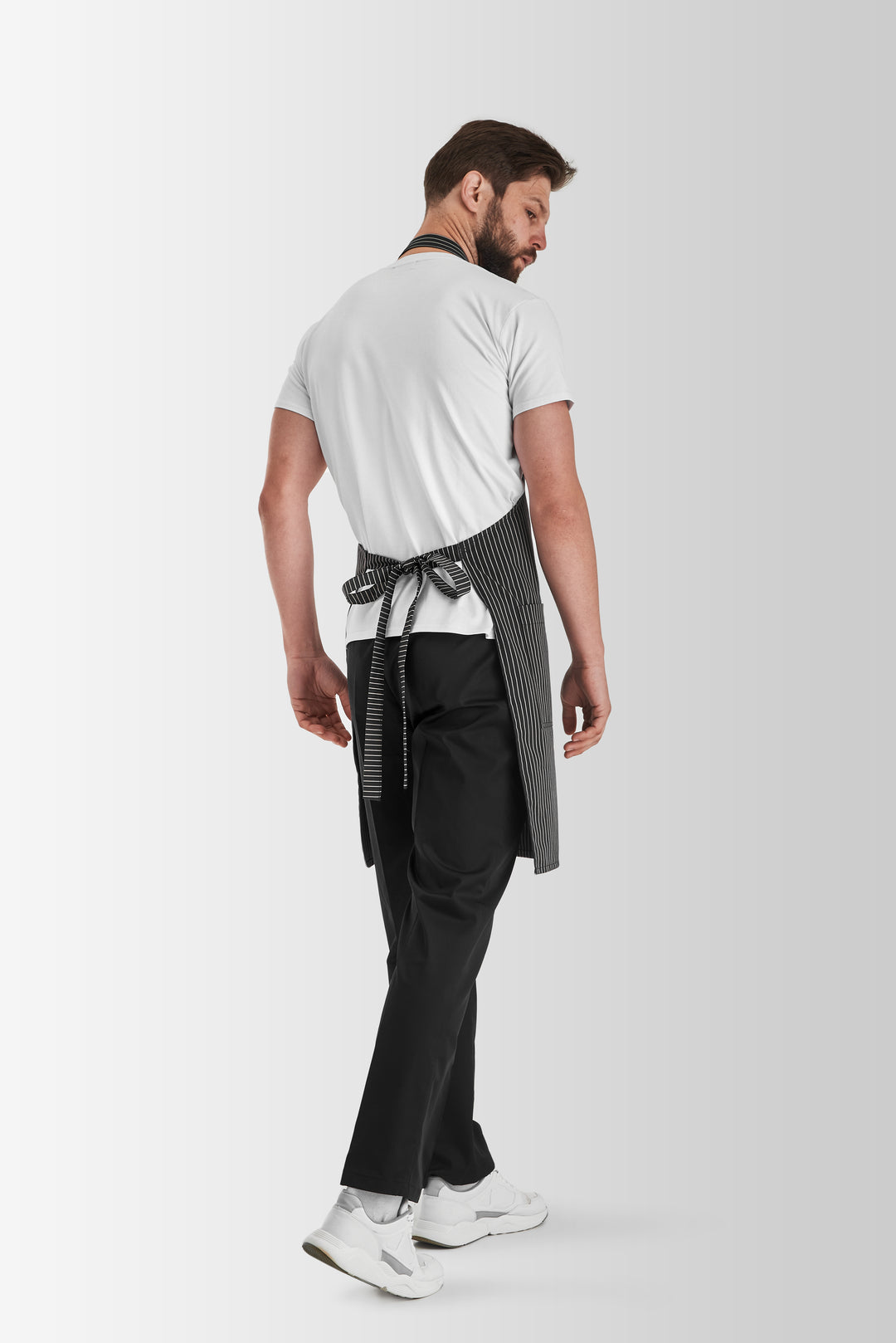 Back view of a man wearing a gray pinstripe bib apron with waist ties
