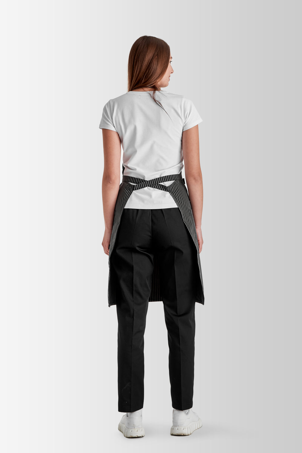 Back view of a woman wearing a gray pinstripe bib apron with waist ties